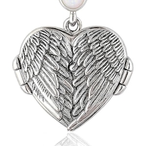 May include: A silver-toned heart-shaped locket pendant with detailed wing designs. The locket opens to reveal space for a photo or keepsake. An oval, white gemstone tops the pendant, adding a touch of elegance. The pendant is designed to be worn as a necklace.