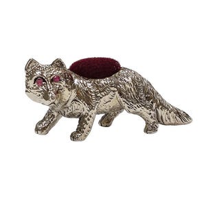 May include: A silver-colored cat-shaped pin cushion with ruby-colored eyes and a burgundy cushion. The cat is in a walking pose, with detailed fur texture. A decorative sewing accessory.