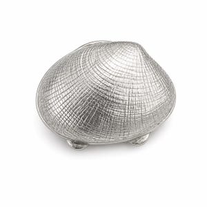 Puede incluir: Un objeto decorativo plateado con forma de concha. La concha tiene una superficie texturizada con un patrón de trama cruzada. El objeto se eleva sobre tres pequeños pies redondeados, y probablemente es una pieza decorativa.
