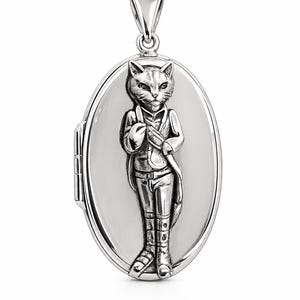 Puede incluir: Colgante de medallón ovalado plateado con un relieve detallado de un gato vestido con un atuendo vintage. El gato lleva una chaqueta, pantalones y botas. El medallón tiene una argolla para una cadena y se abre.