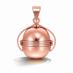 Peut inclure: Un pendentif sphérique en or rose avec un design à charnière. Le pendentif a une boucle en haut pour une chaîne et des accents incurvés décoratifs. Le corps sphérique est divisé en sections avec des lignes horizontales. Le pendentif est conçu pour contenir de petites photos.