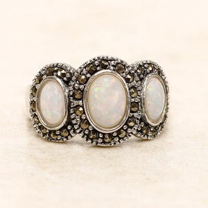 Può includere: Un anello d'argento con tre opali ovali. Ogni opale è incorniciato da piccole pietre rotonde e scure. L'anello ha uno stile vintage, che mette in risalto le pietre preziose e la lavorazione del metallo.