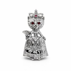 Może przedstawiać: Srebrna figurka kota w koronie z czerwonym klejnotem i szczegółową suknią, trzymająca wachlarz. Kot ma czerwone oczy i stoi wyprostowany. Figurka jest bardzo szczegółowa.