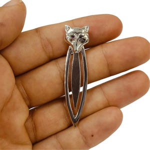 May include: Silver fox bookmark with a detailed design and red eyes. The bookmark is shaped like a fox head with a long, thin body.