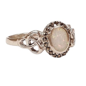 May include: Silver ring with an oval opal gemstone. The ring has a decorative setting with small, dark stones around the opal and a Celtic knot design on the band. A piece of jewellery.