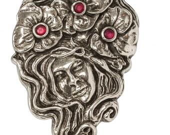 May include: A silver-toned metal pendant featuring a woman's face with flowing hair, surrounded by three flowers with red gemstone centers. The design has an antique, ornate style.