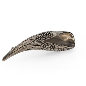 May include: A silver-coloured, stylised leaf-shaped object with a textured, wood-grain appearance. The object has a curved design with floral embellishments and a pointed tip. The interior has a smooth, reflective surface.