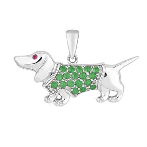 Könnte beinhalten: Ein silberfarbener Anhänger in Form eines Dackelhundes. Der Hund hat einen mit grünen Edelsteinen besetzten Körper und ein rotes Edelsteinauge. Der Anhänger hat eine Schlaufe für eine Kette.