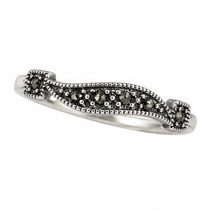 Op de afbeelding: Een zilveren ring met een gebogen ontwerp. Het midden heeft een rij kleine, donkere stenen, begrensd door een kralenpatroon. Vierkante accenten met bijpassende stenen bevinden zich aan elk uiteinde van het gebogen gedeelte. De ring staat tegen een witte achtergrond.