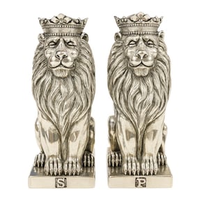 Może przedstawiać: Para srebrnych figurek lwów, każda w koronie. Lwy siedzą na prostokątnych podstawach, jedna oznaczona literą "S", druga "P". Figurki mają szczegółowe grzywy i królewskie wyrazy twarzy, odpowiednie do dekoracji wnętrz.