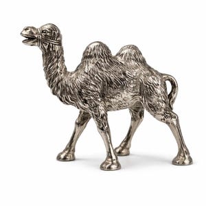 May include: A detailed silver-colored camel figurine. The sculpture features a two-humped camel with intricate detailing on its fur and a bridle. The camel is standing on four legs, with its head turned to the side. The figurine is set against a white background.