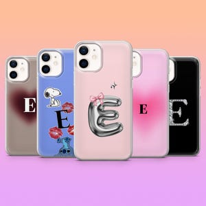 Puede incluir: Cinco fundas para teléfono con la letra "E" en diferentes estilos. Los diseños incluyen un corazón, Snoopy, labios, un diseño metálico en forma de globo con un lazo y un diseño de pedrería. Las fundas son en tonos rosa, azul y negro.