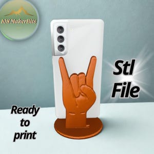 May include: A white smartphone with a brown hand-shaped phone stand. The stand is in the shape of the rock and roll hand gesture. The words "Ready to print" and "Stl File" are also visible.