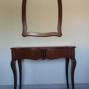 May include: A dark wood console table with two drawers and curved legs, featuring a central carved detail. Above the table hangs a matching rectangular wall mirror with a dark wood frame that mirrors the carved design at the top center.