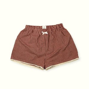 May include: Red and white gingham shorts with a white lace trim and a small white bow at the waist. The shorts have a label that reads "By Lindy".