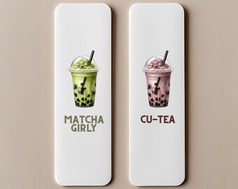 May include: Two white rectangular signs with illustrations of bubble tea. One features a green drink with the text "Matcha Girly." The other shows a pink drink with the text "Cu-Tea." Both drinks have a black straw.