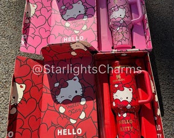 May include: Two Hello Kitty themed insulated tumblers with handles, one pink and one red, each in a matching box. The boxes feature heart patterns and the words "Hello Kitty". The tumblers have the Hello Kitty character and the Stanley brand logo.
