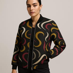 May include: Black bomber jacket with a colourful abstract pattern in gold, burgundy, and cream. The jacket has a ribbed collar, cuffs, and hem, and a silver zip closure. A stylish outerwear piece.