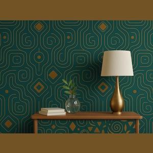 Puede incluir: Una lámpara dorada con una pantalla color crema se encuentra sobre una mesa de madera. Un pequeño jarrón de cristal con hojas verdes y una pila de libros también están sobre la mesa. El fondo es una pared verde azulado con un patrón geométrico dorado.