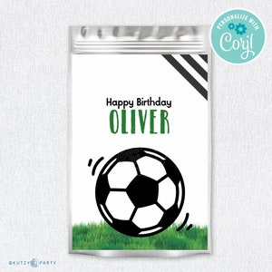 Pode incluir: Uma sacola de presente branca com um design listrado preto e branco. A sacola tem um fundo de grama verde com uma bola de futebol preta rolando sobre ela. O texto "Happy Birthday Oliver" está impresso em verde na sacola.