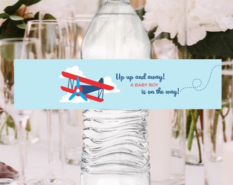 May include: Blue and white baby shower water bottle label with a red and blue airplane illustration. The label says "Up up and away! A baby boy is on the way!"