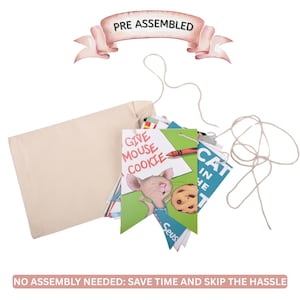 May include: A beige canvas bag with a string closure, holding colorful children's book pages. The pages are shaped like pennants and feature illustrations and text, including "GIVE MOUSE COOKIE" and "CAT IN HE". The banner above reads "PRE ASSEMBLED".