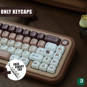 May include: A keyboard with brown, beige, and white keycaps. The keycaps have a retro aesthetic, with a mix of solid colors and small icons. The image includes the text "ONLY KEYCAPS" and "FREE FIDGET TOY".