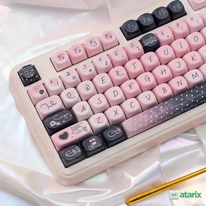 Könnte beinhalten: Eine individuelle mechanische Tastatur mit rosa und schwarzen Tastenkappen. Die Tastenkappen haben weiße Buchstaben und dekorative Symbole. Die Tastatur hat einen beigen Rahmen und einen goldfarbenen Stift in der unteren rechten Ecke.
