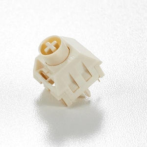 Puede incluir: Un interruptor de teclado mecánico blanquecino. El interruptor tiene un vástago en forma de cruz y una carcasa rectangular con varias aberturas. La parte superior tiene un componente cilíndrico con una hendidura en forma de cruz.