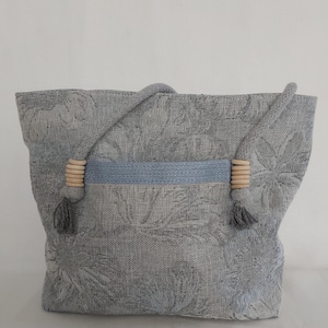 May include: A gray tote bag with a blue stripe and wooden handles. The bag has a floral pattern.