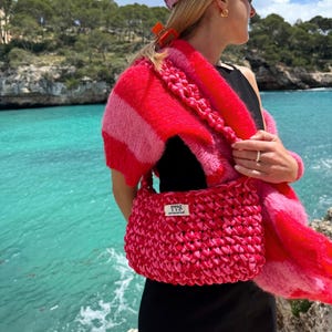 Puede incluir: Un cárdigan de punto a rayas rosa y blanco con un bolso de crochet rosa. El bolso tiene una etiqueta blanca con el texto "YVS, young vintage soul".