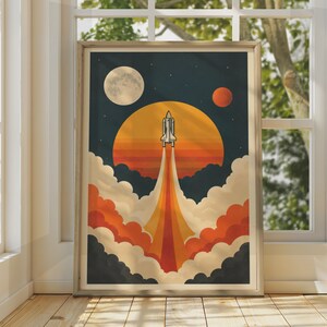 以下が含まれることがあります： 暗い青色の空に向かって打ち上げられるスペースシャトルを描いた額入りアートプリント。シャトルの背後には大きなオレンジ色の太陽があり、オレンジと黄色の排気ガスが尾を引いています。オレンジと濃い灰色の雲がシャトルの基部を取り囲んでいます。