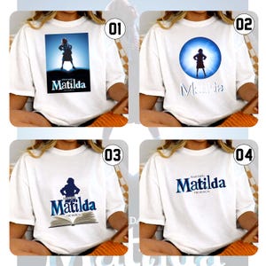 May include: Four white t-shirts with designs from the musical "Matilda." Each shirt has a different graphic: a silhouette of a girl, the musical's title, and the phrase "The Musical." The designs are in blue and white.
