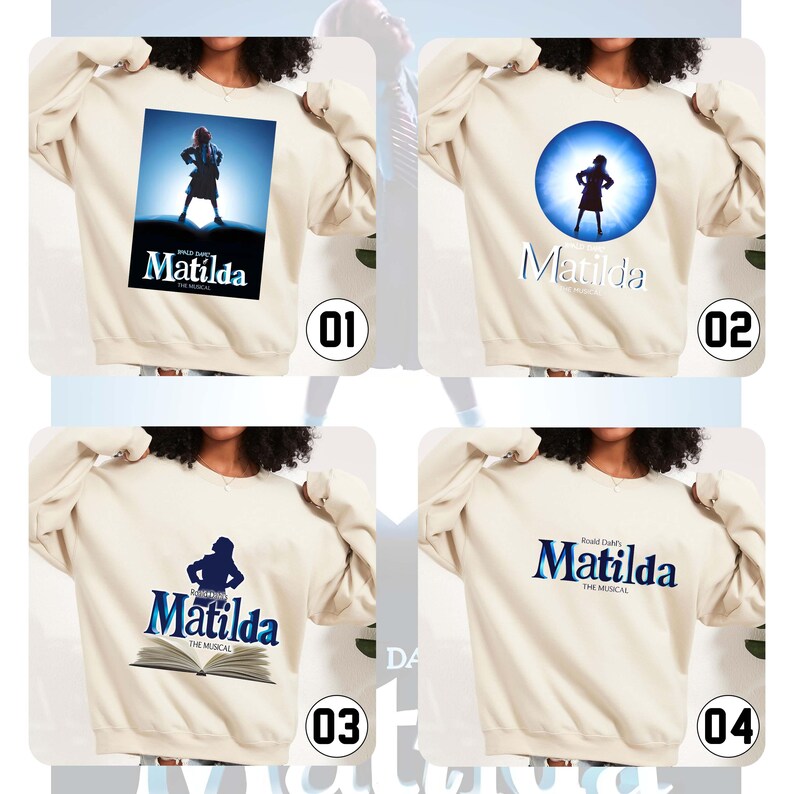 May include: Cream-coloured sweatshirts with designs from the musical "Matilda". The designs include a girl on a stage, a silhouette in a blue circle, and the musical's logo in blue and white.