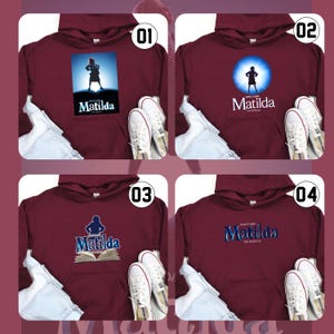 May include: Four maroon hoodies, each with a different design related to the musical "Matilda". Designs include a silhouette, a spotlight, an open book, and the musical's logo. White trainers and blue jeans are displayed with each hoodie.