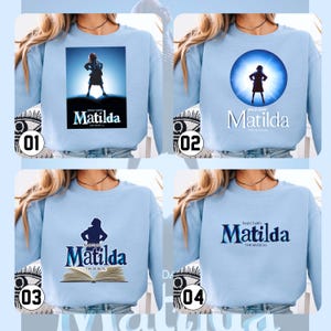 May include: Pale blue sweatshirts with different designs promoting the musical "Matilda". The designs include a silhouette of a girl, a girl in a spotlight, and the musical's logo. The text "Matilda The Musical" is also visible on the sweatshirts.