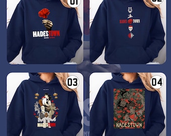May include: Four navy blue hoodies with different designs. One features a red flower, another has a harp and skull, the third has a group of figures, and the last has a floral design. Each hoodie has the text "HADESTOWN".