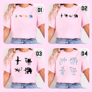 May include: Four pink t-shirts with different graphic designs. Each shirt features a unique set of stylized animal or symbol illustrations in various colors. The shirts are displayed on a person.