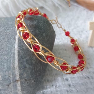 May include: A gold wire-wrapped bracelet featuring a series of faceted, round, translucent red beads. The metallic wire is intricately coiled around each bead, forming a continuous, open-work lattice structure that secures with a simple hook clasp.