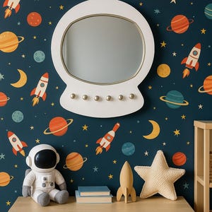 May include: A white astronaut helmet-shaped mirror hangs on a navy blue wall decorated with planets, rockets, moons, and stars. A wooden chest of drawers holds a plush astronaut, books, a wooden rocket, and a star-shaped cushion.