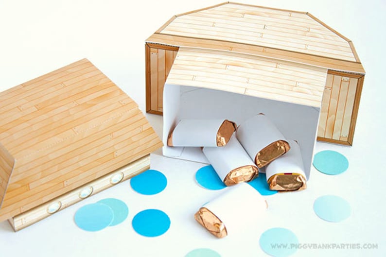 May include: A wooden ark-shaped box with a hinged lid, partially open, revealing several wrapped candies. The box is made of light brown wood-grain patterned paper. Blue confetti dots the white surface. The website address "www.piggybankparties.com" is visible.