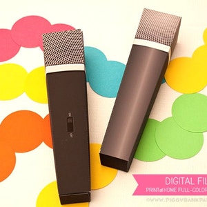 Puede incluir: Se muestran dos cajas con forma de micrófono marrón oscuro con tapas de malla plateada y detalles en blanco. Las cajas están sobre una superficie blanca con confeti de colores. Una caja tiene un interruptor de encendido/apagado. La imagen incluye el texto "DIGITAL FILE".