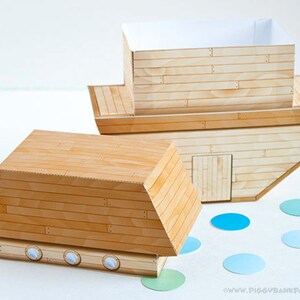 May include: Two wooden toy boats with a light wood grain pattern. One boat is upright, showing the interior, and the other is on its side. Blue and green confetti dots are scattered around the boats.