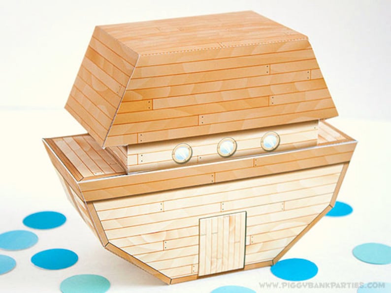 May include: A paper craft of Noah's Ark, featuring a light brown wooden plank design. The ark has a rectangular base and a sloped roof. It includes three round windows and a small door. Blue confetti dots are scattered around the ark.