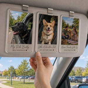 Könnte beinhalten: Ein Auto-Sonnenblenden-Organizer mit drei durchsichtigen Acryl-Fotorahmen und Metallclips. Die Rahmen zeigen Fotos von Hunden und einer Familie mit dem aufgedruckten Text: My Ride Buddy, Little Adventure Pal und Home Travels With Us sowie Untertiteln.