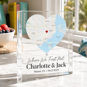 Könnte beinhalten: Ein klarer, rechteckiger Acrylblock mit einer herzförmigen Karte von Miami, Florida, und einer roten Herzmarkierung. Unter der Karte steht der Text: Where We First Met, Charlotte & Jack, Miami, FL | 27.08.2023, mit einem kleinen Herzsymbol darüber.