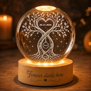 May include: A clear glass sphere lamp featuring an internal laser-etched tree with heart-shaped branches, the date 09.21.2026, and the names Olivia and Noah. The light sits on a round wooden base engraved with the text Forever starts here.