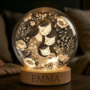 May include: A glowing glass sphere lamp with a wooden base. Inside, a mother and two children are embraced, surrounded by floral designs. The base is engraved with the name "EMMA". The lamp emits a warm, inviting light.