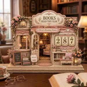 Könnte beinhalten: Ein Miniatur-Buchladen-Diorama mit dem Titel Olivia's Reading Room, einem Schild mit der Aufschrift BOOKS READ THIS YEAR und einer Anzeige mit der Zahl 287. Das Modell hat rosa Blumenakzente, ein kleines Kreidetafelschild und Innenbeleuchtung.