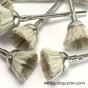 Könnte beinhalten: Ein Satz von zehn kleinen, weißen Bürsten mit silbernen Metallgriffen. Die Bürsten sind mit einer Schraube an den Griffen befestigt. Die Bürsten liegen auf einer weißen Oberfläche.